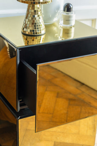 Close-up of a gold bedside table with the top drawer open, styled with various accessories.