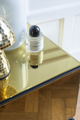 Close-up of the top of a gold bedside table, styled with a perfume bottle and other accessories.