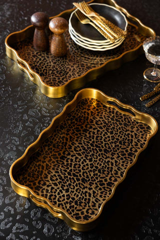The Set of 2 Gold & Leopard Serving Trays styled with various dining accessories.