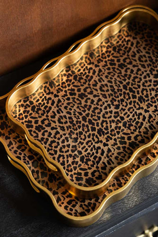 Close-up of the Set of 2 Gold & Leopard Serving Trays on a dark wooden surface.