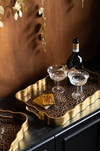 The Set of 2 Gold & Leopard Serving Trays styled on a dark sideboard with some playing cards, cocktail glasses and a bottle.