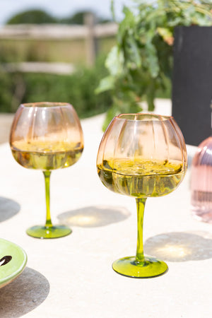 The Set of 2 Pink & Green Gin Glasses on an outside dining table.