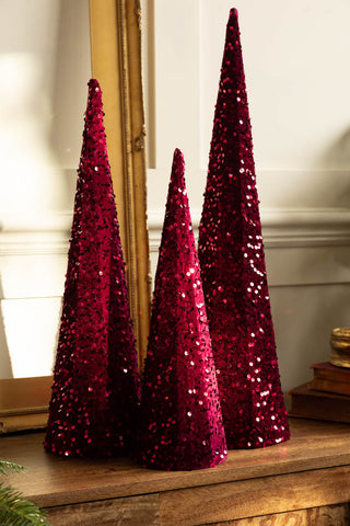 The Set of 3 Burgundy Sequin Christmas Cones shown on a wood sideboard against a mirror. 