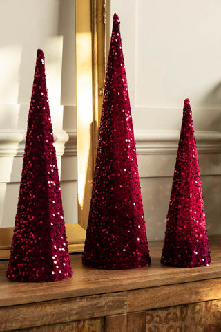 The Set of 3 Burgundy Sequin Christmas Cones shown in a row on a wood sideboard. 