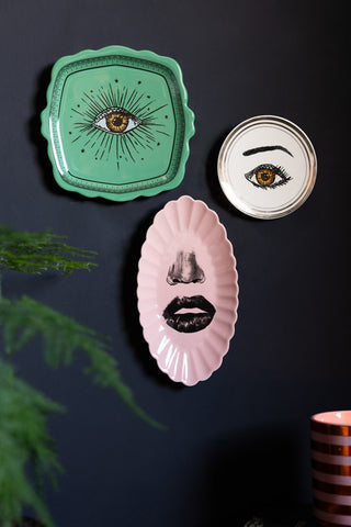 The Set of 3 Colourful Face Wall Plates displayed on a dark wall above a lit candle and a plant.