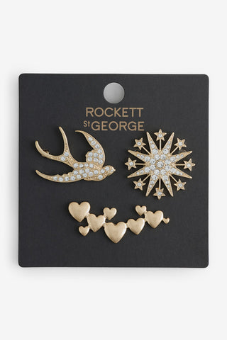The Set of 3 Gold Stars & Birds Brooch Pack, with the gold jewelled bird, star and gold heart brooches shown against a black Rockett St George branded jewellery holder. 