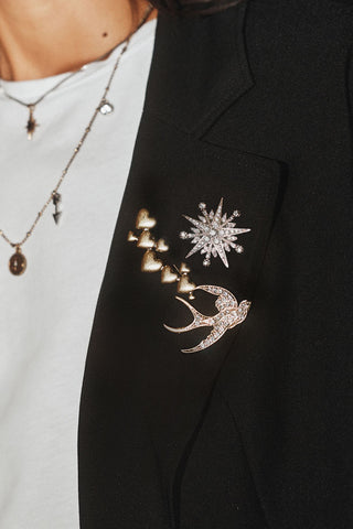 The Set of 3 Gold Stars & Birds Brooch Pack, with the gold hearts, jewelled star and jewelled swallow bird brooches shown on the lapel of a black jacket. 