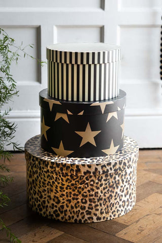The Set of 3 Signature Storage Boxes in Stripes, Stars & Leopard Print shown against white panelled walls. The smallest box is a monochrome stripe, the medium is a black and beige star design and the largest box is leopard print. 