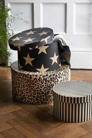 The Set of 3 Signature Storage Boxes in Stripes, Stars & Leopard Print shown against white panelled walls with the star box open and a scarf hanging over the side. 