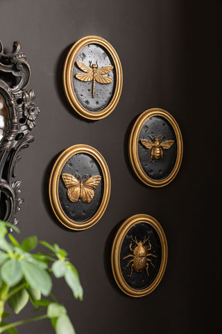 The Set of 4 Black & Gold Entomology Wall Art styled against a black wall. 