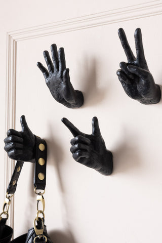 Four hand shaped wall hooks on a plain wall with a handbag hanging from it.