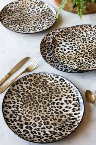 The Set of 4 Leopard Print Dinner Plates shown on a marble tabletop with gold cutlery and a plant in the background. 