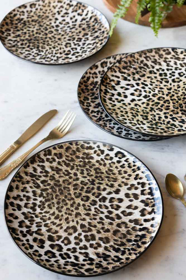 The Set of 4 Leopard Print Dinner Plates shown on a marble tabletop with gold cutlery and a plant in the background. 