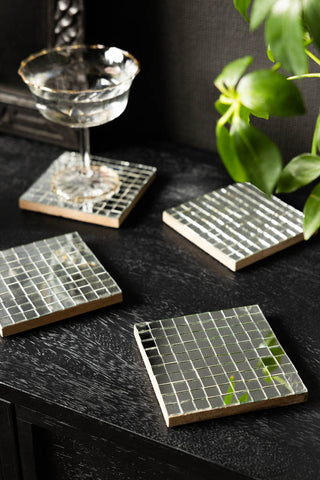 The Set of 4 Silver Disco Mosaic Coasters shown on a sideboard with a champagne cocktail glass. 