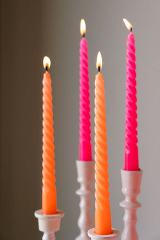 The Set of 4 Twisted Dinner Candles in Hot Pink & Orange displayed lit in candlestick holders of varying heights.