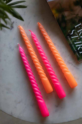 The Set of 4 Twisted Dinner Candles in Hot Pink & Orange displayed together on a white marble table with a magazine and a plant.