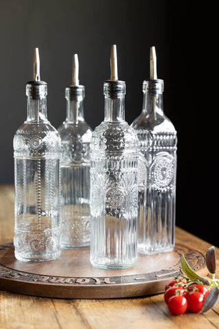 The Set of 4 Vintage-Style Oil Dispenser Glass Bottles displayed on a wooden serving board next to some tomatoes.