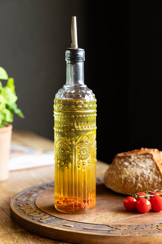 One iof the Set of 4 Vintage-Style Oil Dispenser Glass Bottles styled with oil inside, displayed on a wooden serving board with some bread and tomatoes.