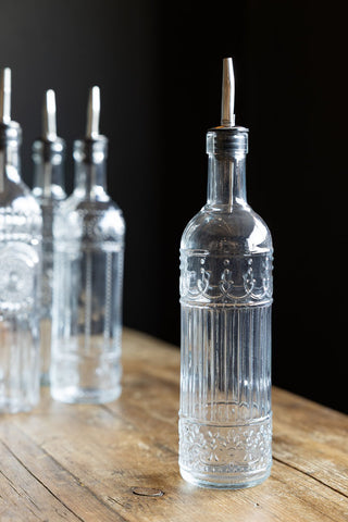One of the Set of 4 Vintage-Style Oil Dispenser Glass Bottles displayed on a wooden surface, with the other three in the background.