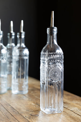 One of the Set of 4 Vintage-Style Oil Dispenser Glass Bottles on a wooden surface, with the other three styled in the background.
