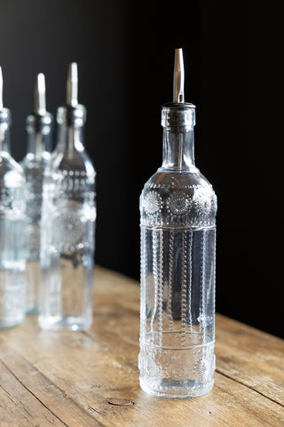 An oil dispenser bottle with a circle design on a wooden surface, styled with three other bottles in the background.