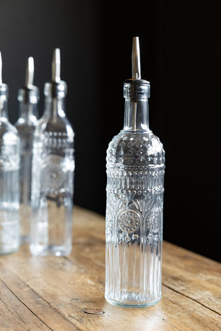 A decorative oil pourer bottle displayed on a wooden surface, with three other bottles displayed in the background.