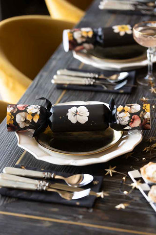 Lifestyle image of the set of 6 dark floral luxury Christmas crackers on a tablescape, with cutlery, glassware, napkins and plates. 
