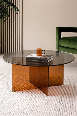 The Seventies Amber Glass Oval Coffee Table styled with a mug and some books on, displayed in a living room.