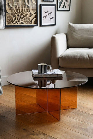 The Seventies Amber Glass Oval Coffee Table with a mug and some magazines on, styled in a living room.
