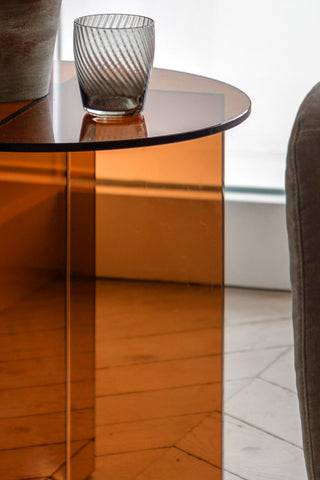 Close-up of the Seventies Amber Glass Side Table styled with a plant pot and tumbler on, next to a sofa.