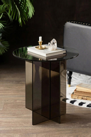 The Seventies Smoked Glass Side Table styled with a book and some accessories on, displayed next to a sofa and plant.