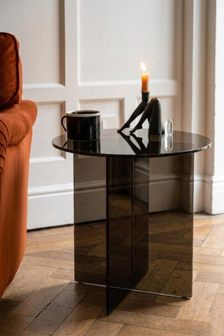 The Seventies Smoked Glass Side Table with a mug and candle on, styled next to a sofa.