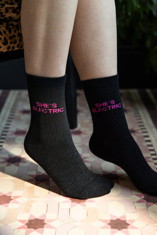 The She's Electric Cotton Glitter Socks shown against pink star tile-effect flooring. 