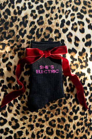 The She's Electric Cotton Glitter Socks shown with a red bow against a leopard print background. 