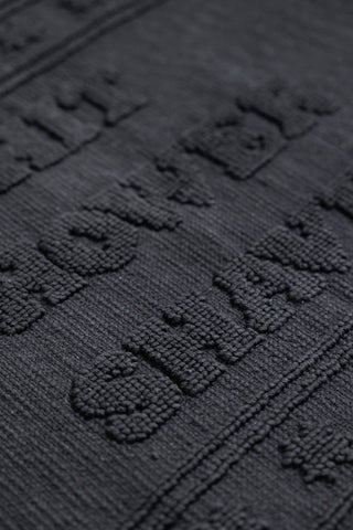 A detail image showing the raised textured text on the Shit Shower Shave Black Bath Mat. 