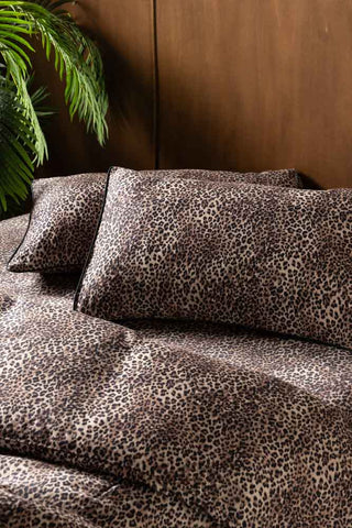 The Signature Leopard Print Cotton Sateen Bedding Set styled on a bed with a large plant in the background.