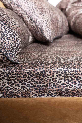 The Signature Leopard Print Cotton Sateen Fitted Sheet styled on a bed with some matching pillows and bedding.
