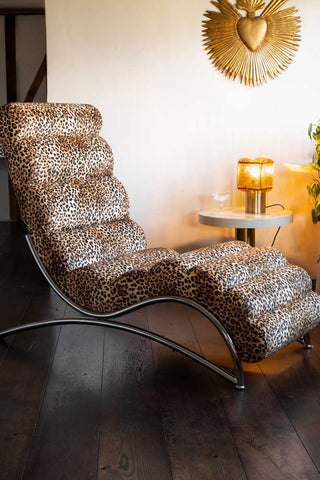 The Signature Leopard Print Lounger Chair shown again neutral walls with dark wood flooring and a gold milagro wall art piece on the wall. 
