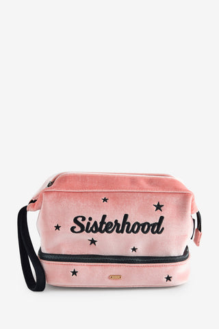 The Sisterhood Blush Pink Velvet Washbag shown against a white background. The product is a pale pink velvet washbag embroidered with black stars and the word "sisterhood" it has two zip compartments. 