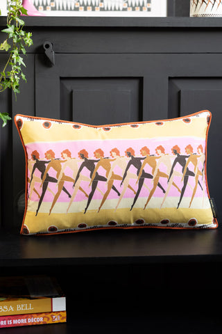 The Sisterhood Charity Rectangular Cushion  styled on a bench surrounded by some accessories and greenery.