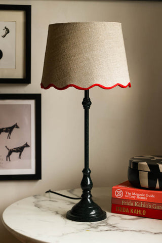 Lifestyle image of the Slim Table Lamp with Red Scalloped Linen Shade displayed on a marble table with other home accessories.