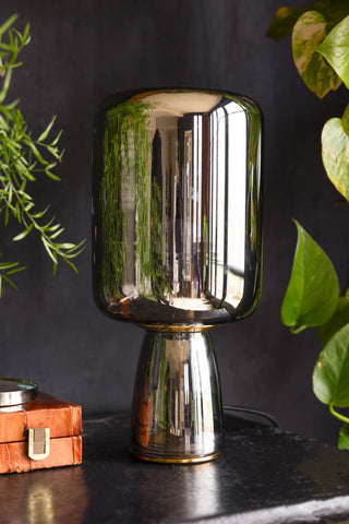 Lifestyle image of the Smoked Table Lamp displayed on a black sideboard alongside other home accessories and plants in the background.