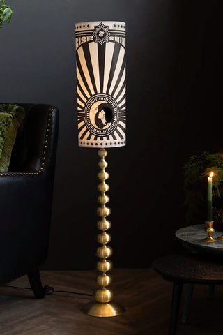 The Solar Goddess Bobbin Floor Lamp in the corner of a room in front of some black furniture.
