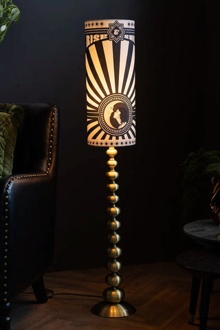 The Solar Goddess Bobbin Floor Lamp in front of a black sideboard and plant.