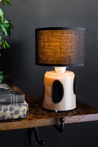 The Spotted Glass Rechargeable Table Lamp switched on and displayed on a leopard print shelf with some books and some greenery.