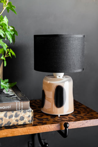 The Spotted Glass Rechargeable Table Lamp on a shelf with some greenery and books.