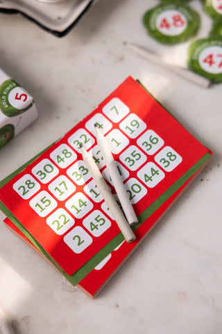 The cards and pencils in the Sprout Bingo Christmas Party Game on a white table.