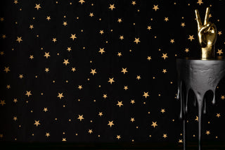 Black wallpaper with gold falling stars, there is a drip table in the foreground with a peace hand. 