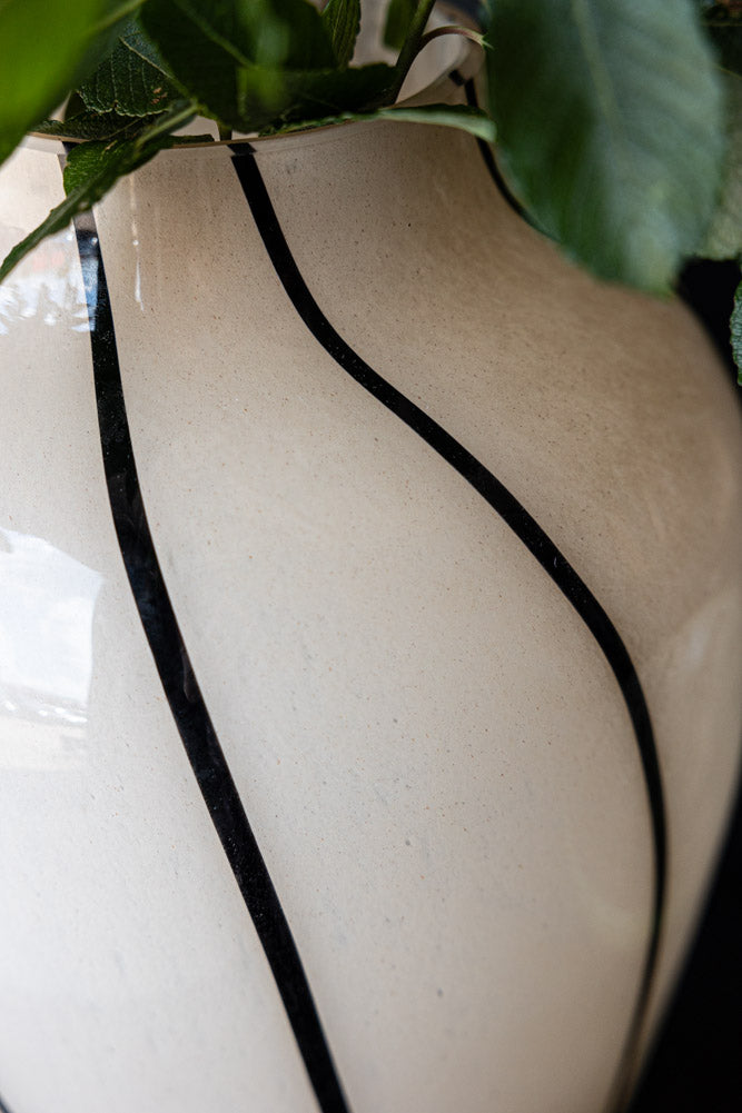 A close up of the line detailing on the Statement Monochrome Swirl Vase with a green plant in it. 