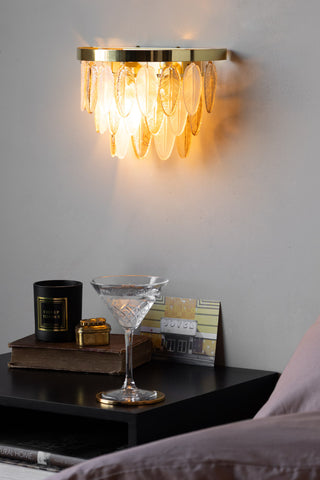 The Stunning Art Deco Glass Feather Wall Light switched on, styled on the wall above a bedside table with various accessories on.